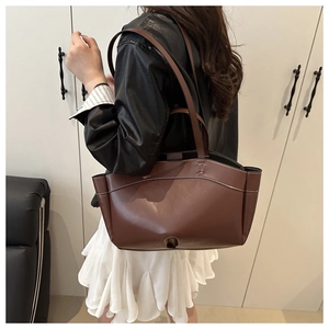 Detail of large brown leather tote bag with contrast stitching and handle hardware