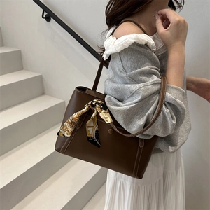 Brown leather tote bag with silk scarf accessory worn by model in minimalist urban setting