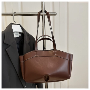Detailed close-up of brown leather tote bag with white contrast stitching and cut-out design