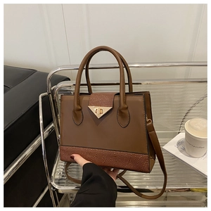 Detail of a brown patchwork handbag featuring lychee texture and gold triangle lock buckle