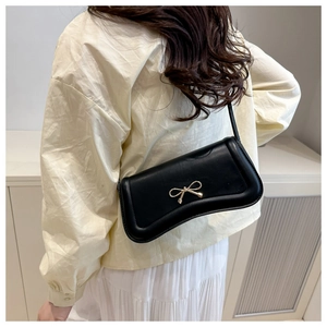 Detailed view of black leather shoulder bag with gold metal bow on minimalist model outfit
