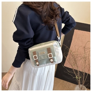 Detail showing the green and cream canvas crossbody bag with decorative brown buckle straps