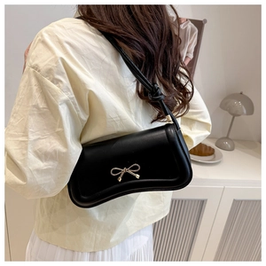 Detail of black crossbody bag with gold bow ornament and elegant knotted strap