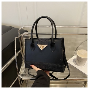 Detail of black crossbody bag with textured leather, gold clasp, and cylindrical handles