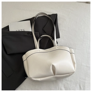Detail of minimalist cream tote bag showing black contrast edges and pleated base design
