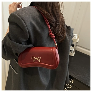 Detail of dark red leather shoulder bag with gold bow clasp worn with a grey blazer