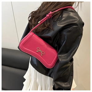 Detail of rose red crossbody bag featuring gold bow buckle and knotted shoulder strap