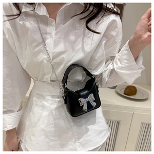 Mini black leather crossbody bag with silver bow buckle worn in an elegant lifestyle setting