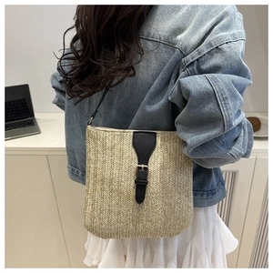 Detail of woven straw shoulder bag with black leather flap and metal buckle on casual outfit