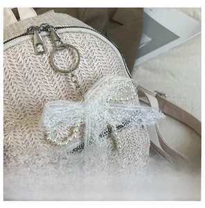 Close-up of beige woven straw backpack featuring pearl charm and white lace bow detail