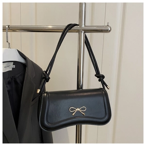 Close-up of black baguette bag with gold butterfly clasp and knotted shoulder strap
