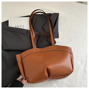 Detail of caramel leather tote bag showing white contrast stitching on grey blazer