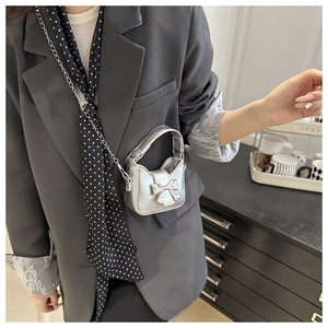 Close-up of matte silver micro bag with bow detail and silver chain strap on grey blazer