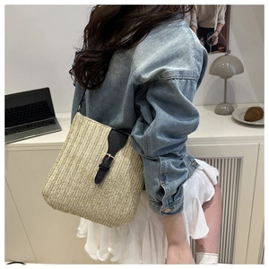 Detail of hand-woven straw shoulder bag with black leather strap and buckle for beach