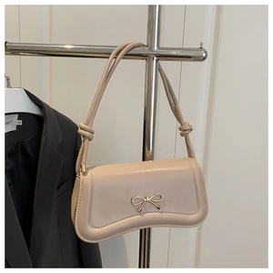 Close-up of beige baguette bag with gold bow buckle and knotted shoulder strap detail