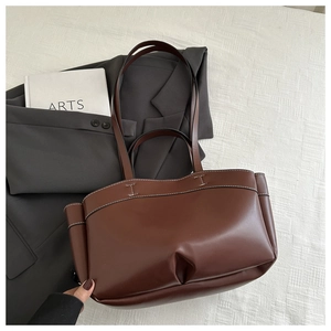Detail view of brown tote bag featuring white contrast stitching and I-shaped handle seams