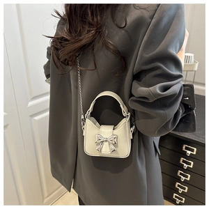 Mini bow handbag in creamy white leather with silver chain strap worn with a grey blazer