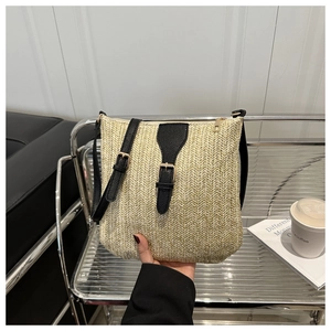 Detail of hand-woven straw crossbody bag with black leather strap and gold hardware