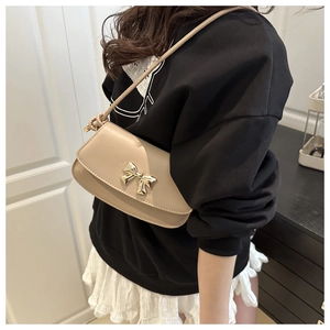 Détail d'un sac à bandoulière beige avec nœud doré porté par un mannequin en intérieur