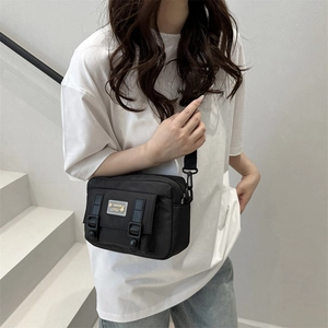 Black canvas mini messenger bag with double decorative buckle straps on white T-shirt