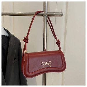 Detail of red leather underarm bag with elegant gold bow buckle and knotted strap