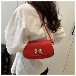 Détail du sac à bandoulière en cuir rouge avec un fermoir nœud doré décoratif sur le rabat
