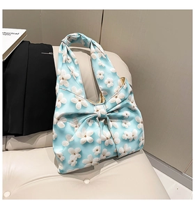 Detail of light blue floral handbag featuring a decorative 3D bow on soft fabric texture