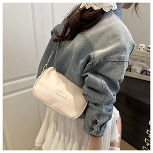 Close-up of beige crossbody bag with gold hardware worn with a denim jacket