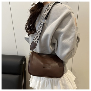 Detail of dark brown leather crescent bag with wide geometric woven shoulder strap and metal hardware