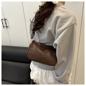 Detail of dark coffee pillow bag with embossed fashion label on textured leather