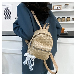 Detail of straw mini backpack with lace pearl charm and metal zipper on textured woven body