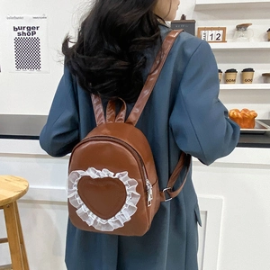 Brown leather backpack with heart lace design worn by model in a cozy cafe setting