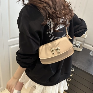Sac à bandoulière beige minimaliste avec nœud en métal doré porté par un mannequin