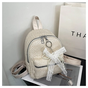 Detail of summer straw backpack featuring white lace bow and elegant pearl chain accessory