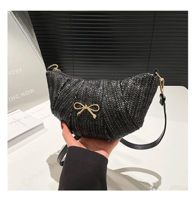 Detail showing the woven texture of the black crescent bag with golden metal bow accent