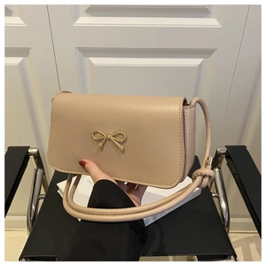 Close-up of beige handbag featuring a decorative gold bow buckle and knotted strap detail