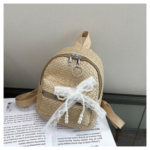 Detailed straw backpack with white lace bow and pearl accents on a magazine