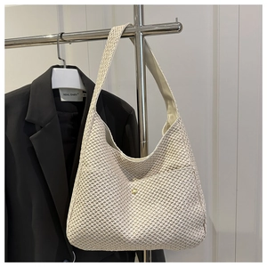 Close-up of beige woven tote bag featuring a round gold buckle and mesh texture