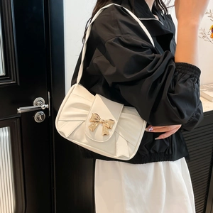 Sac à bandoulière en cuir plissé blanc avec nœud doré porté par un modèle