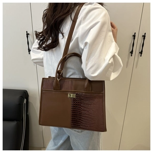 Detail of a brown tote with crocodile pattern texture and a golden twist lock closure