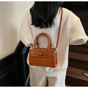 Close-up of caramel crocodile pattern handbag with silver metal twist lock and leather strap