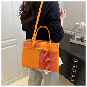 Detail of orange crocodile pattern patchwork tote with golden metal twist lock closure