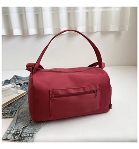 Detail of burgundy nylon travel bag featuring a front zipper pocket and side branding label