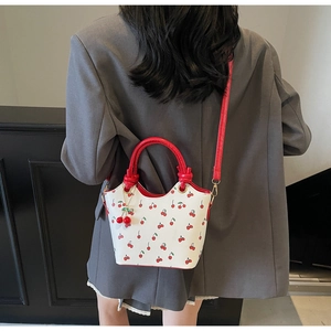 Détail du sac seau blanc à motif cerise avec anses nouées et charms cerises en 3D
