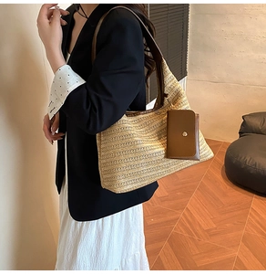 Detail of a large woven straw tote bag with brown leather strap and mini pouch charm