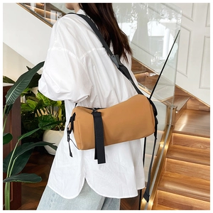 Model wearing a khaki cylindrical crossbody bag made of durable matte PU leather