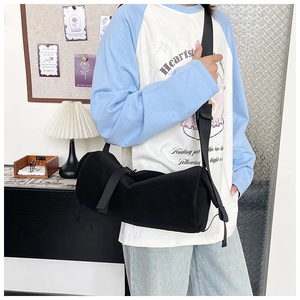 Detail of a black cylinder crossbody bag with adjustable wide strap shown on a model