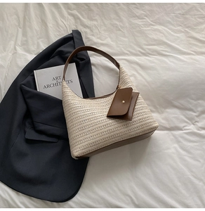 Detail of straw woven tote with brown leather handles and small charm on white fabric