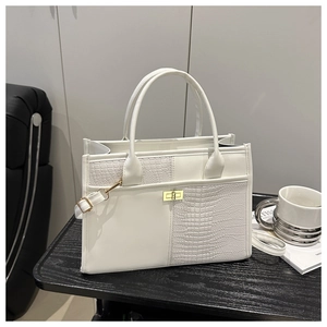 Detail view of white tote bag featuring crocodile embossed leather and gold twist lock