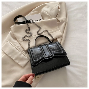 Details einer schwarzen Handtasche mit Krokodilprägung und Kettenriemen auf einem Blazer
